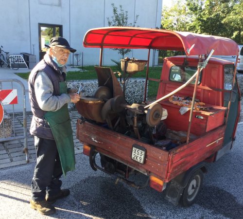 Il moletta (Arrotino) con l'Ape Piaggio rossa che sta affilando delle forbici